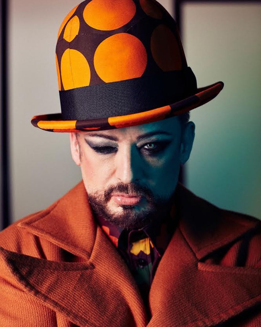 Portrait of Boy George wearing an orange and brown polka dot bowler hat and rust coat, photographed by Leigh Keily