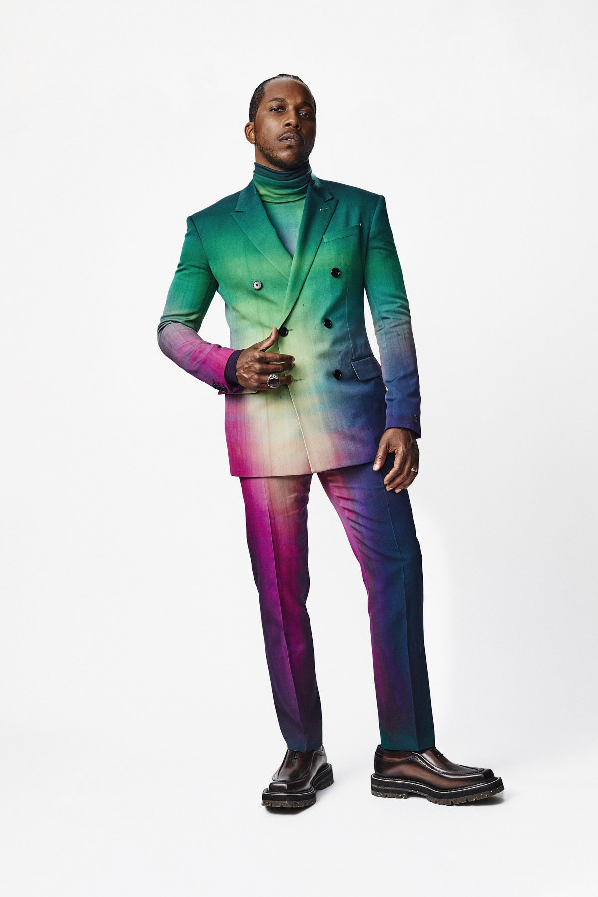 Full body studio shot of an adult male in a colorful suit. The jacket is a double breasted blazer with pants and leather shoes.