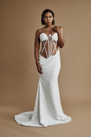 Woman wearing a strapless white structured gown with vertical boning against a plain neutral brown backdrop.
