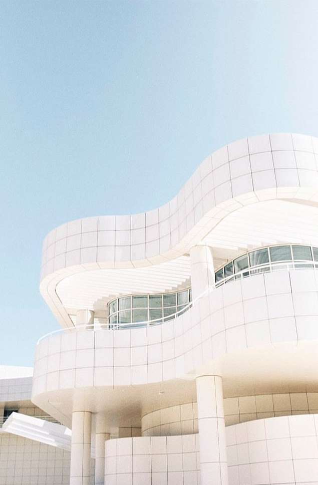 Architectural view of a modern white building with curved walls and windows under a pastel blue sky, clean lines, and minimalist design.