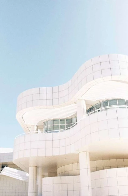 Architectural view of a modern white building with curved walls and windows under a pastel blue sky, clean lines, and minimalist design.