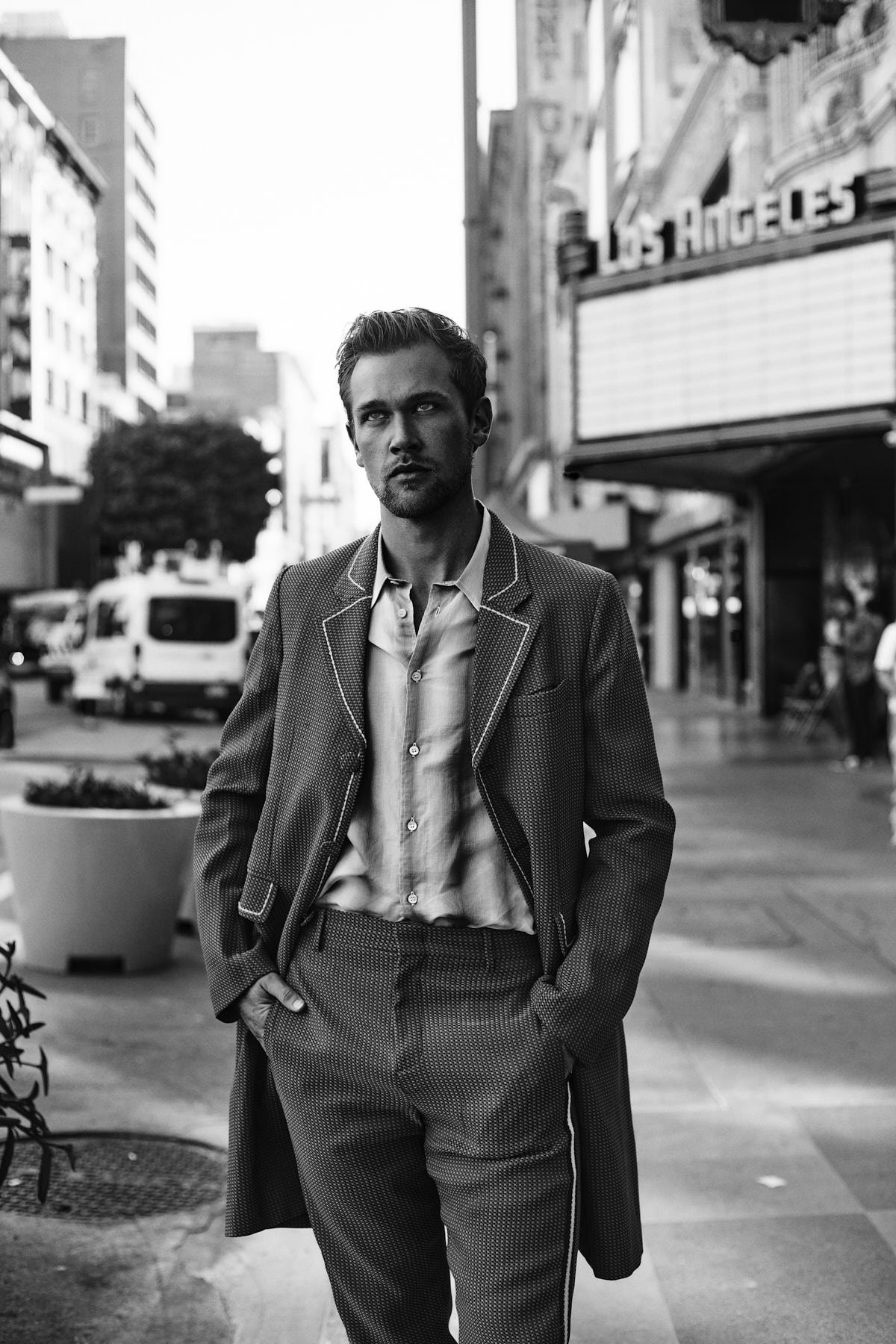 Black and white outdoor portrait of a man in a striped suit standing on a city street in front of a theater in Los Angeles, California.