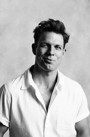 Monochrome portrait of a man with dark hair wearing a white collared shirt against a light textured background