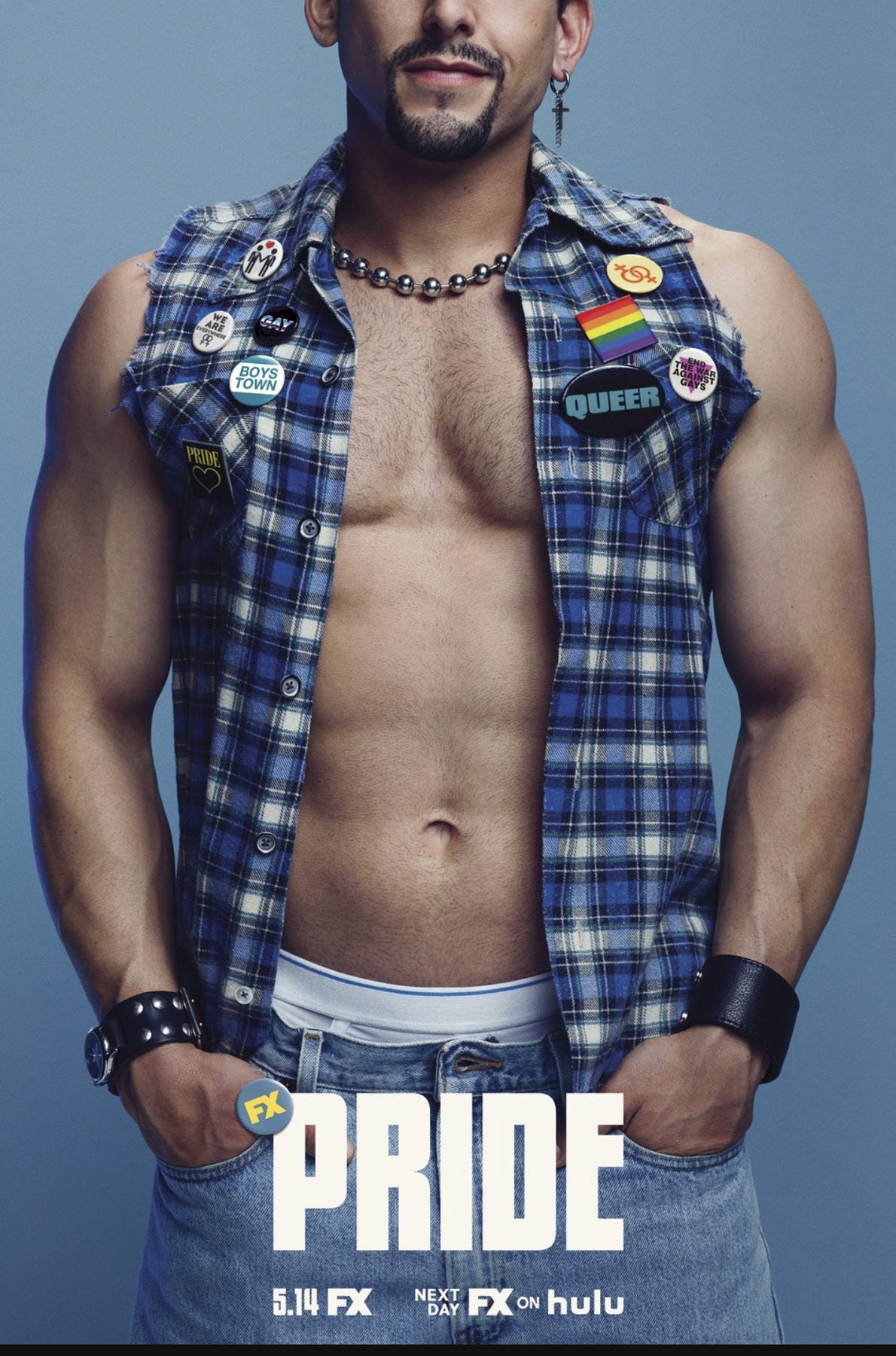 Promotional portrait of muscular adult man wearing a plaid vest with buttons, wristbands, and jeans against a light blue background.