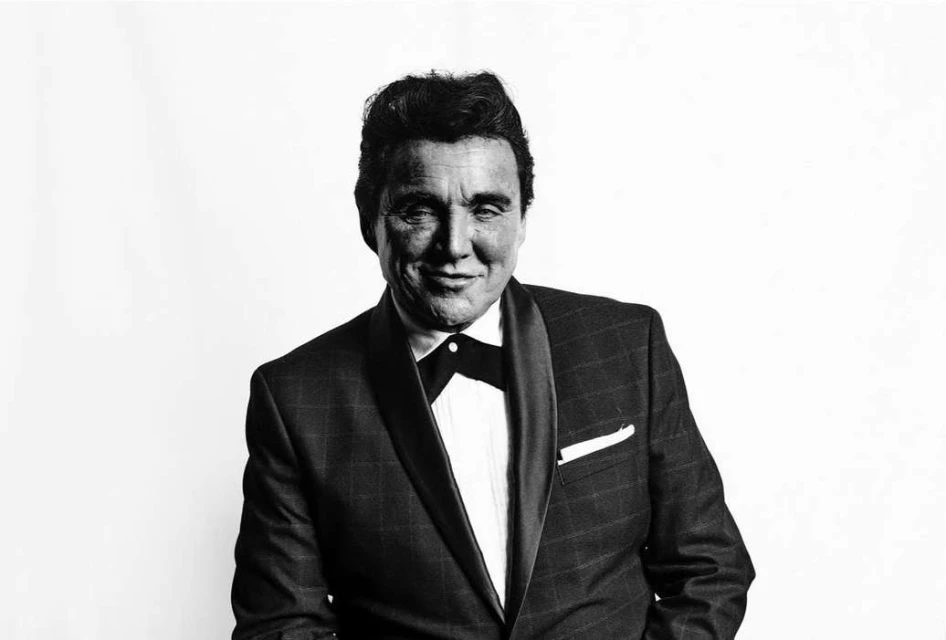 Monochrome portrait of a smiling man in a suit and bow tie against a plain background, capturing a classic and formal aesthetic.