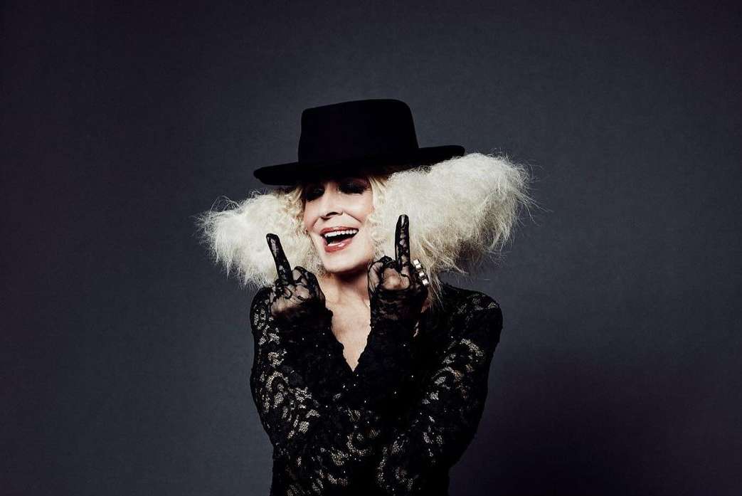 Elderly woman wearing a black hat, lace top, and gloves, making a hand gesture, photographed by Leigh Keily.