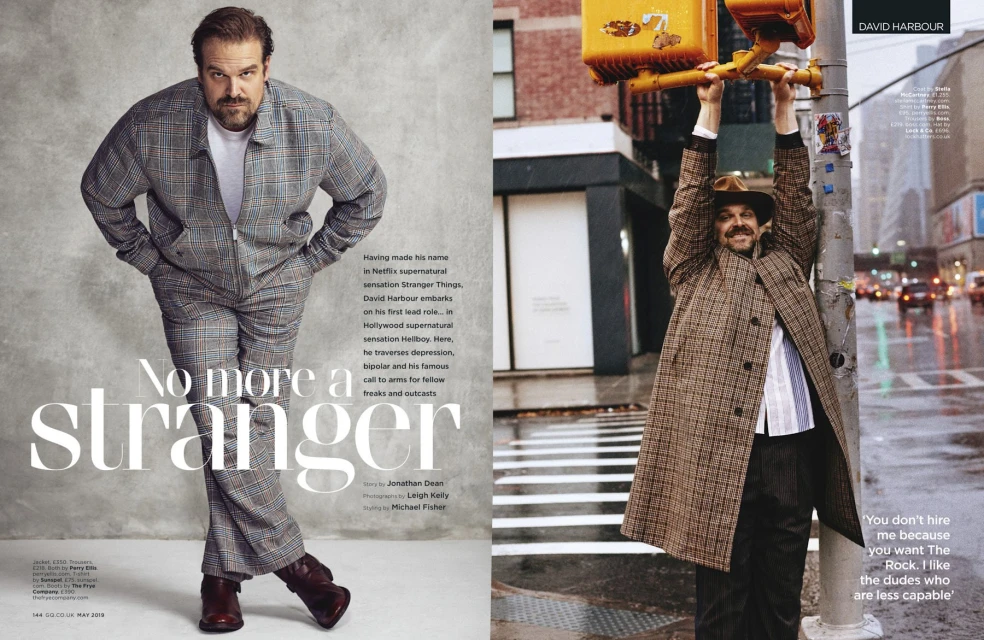 David Harbour wears a plaid suit and leather boots inside a magazine spread. He also hangs from a traffic signal in an urban setting.