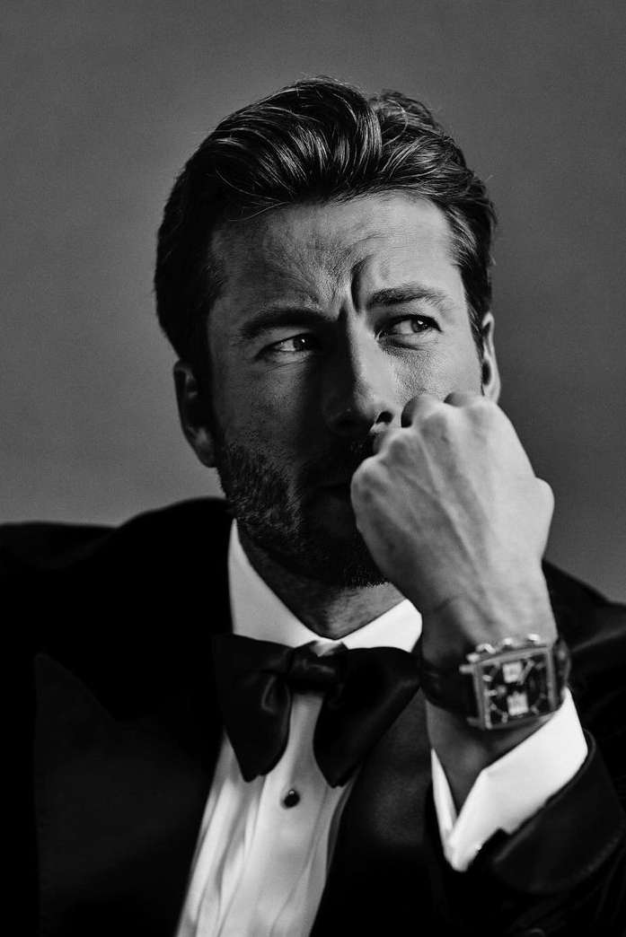 Monochrome portrait of a man in a tuxedo and bow tie wearing a wristwatch with his hand near his face by Leigh Keily