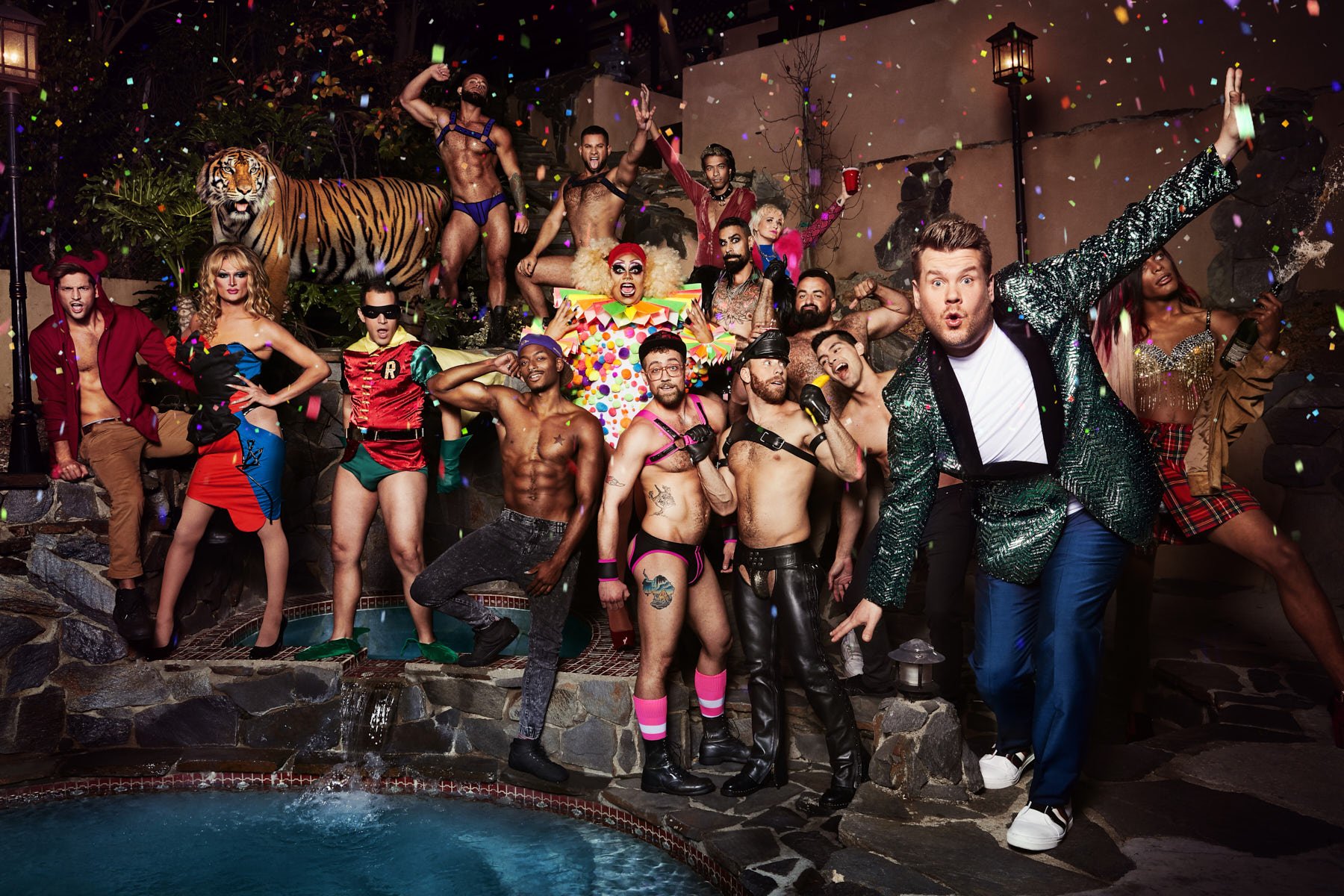 Large group of diverse people in costumes and various states of undress, confetti, and a faux tiger statue at an outdoor party.