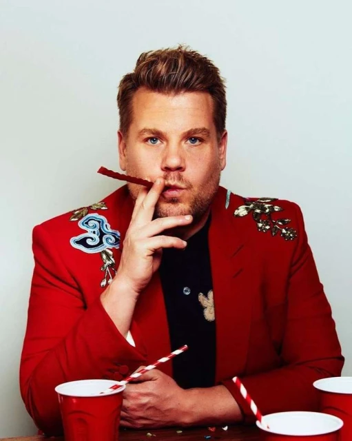 Portrait of a man in a red floral blazer posing with a Twizzler in his mouth and red cups with straws on the table.