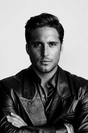 Portrait of Diego Boneta with folded arms wearing a dark leather jacket against a light background by Leigh Keily