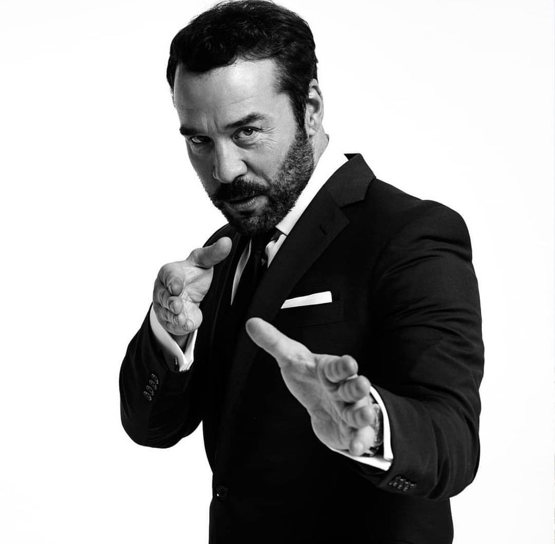 Monochrome portrait of Jean Dujardin in a black suit extending his hands forward