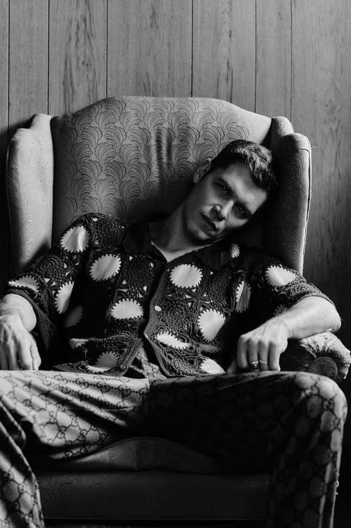 Monochrome portrait of a man in patterned pajamas sitting in an armchair against a wood-paneled wall.