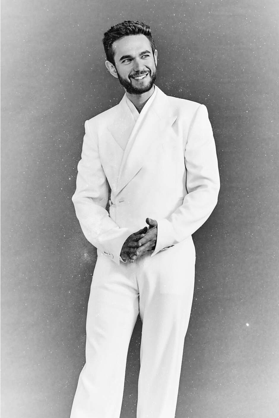 Man wearing a white double breasted suit smiling against a textured grey studio background