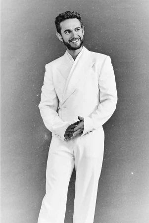 Man wearing a white double breasted suit smiling against a textured grey studio background
