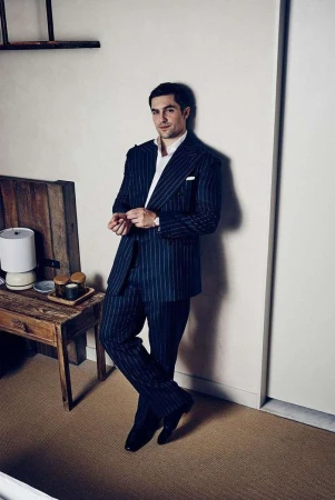 Man in dark pinstripe suit leaning against a wall in a room by photographer Leigh Keily