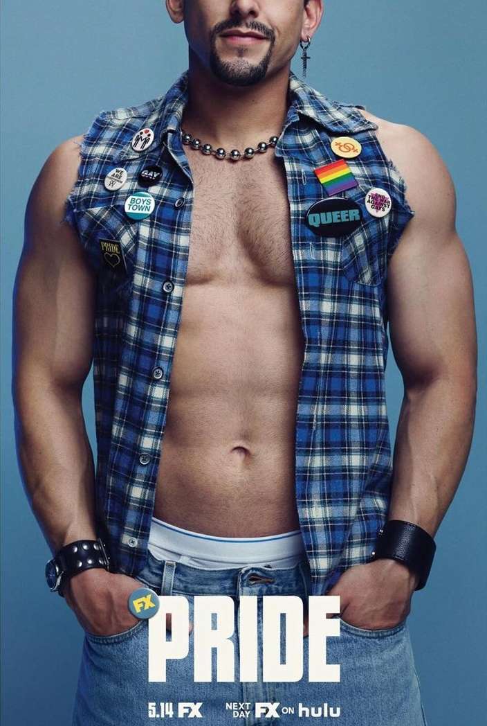 Close-up shot of adult male with bare chest, wearing open plaid shirt and jewelry, with hands in jean pockets, against light blue background.