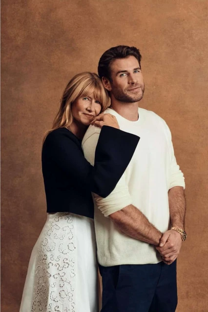 Portrait of adult male and adult female, arm around shoulder, wearing formal wear against a solid brown backdrop in a photo studio.