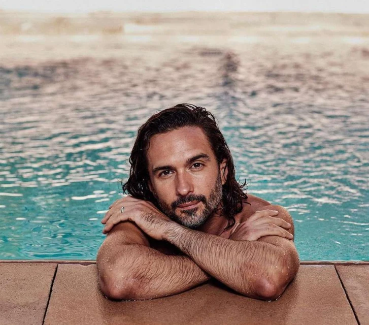 Adult male in a swimming pool with arms crossed, showcasing a relaxed pose and a calm expression, water and light background.