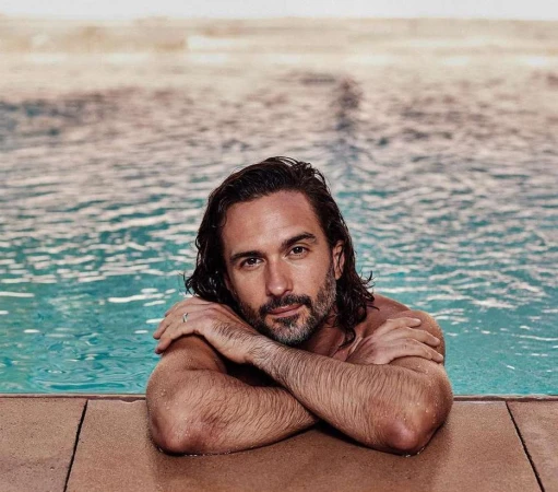 Adult male in a swimming pool with arms crossed, showcasing a relaxed pose and a calm expression, water and light background.
