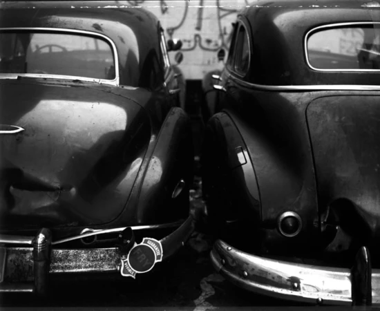Monochrome image showcasing the rear of two vintage cars parked closely together, emphasizing their classic design and bumper details.