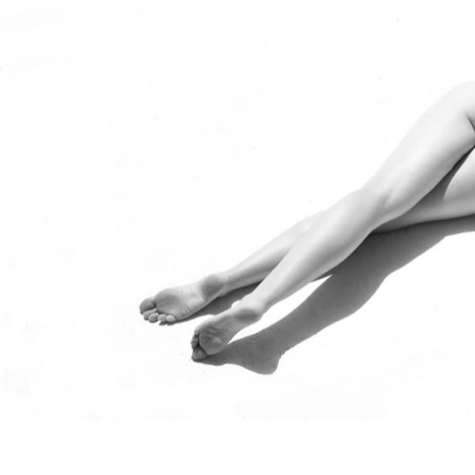 Black and white studio image of a woman's legs extended against a seamless white background, emphasizing form and minimalist aesthetics.
