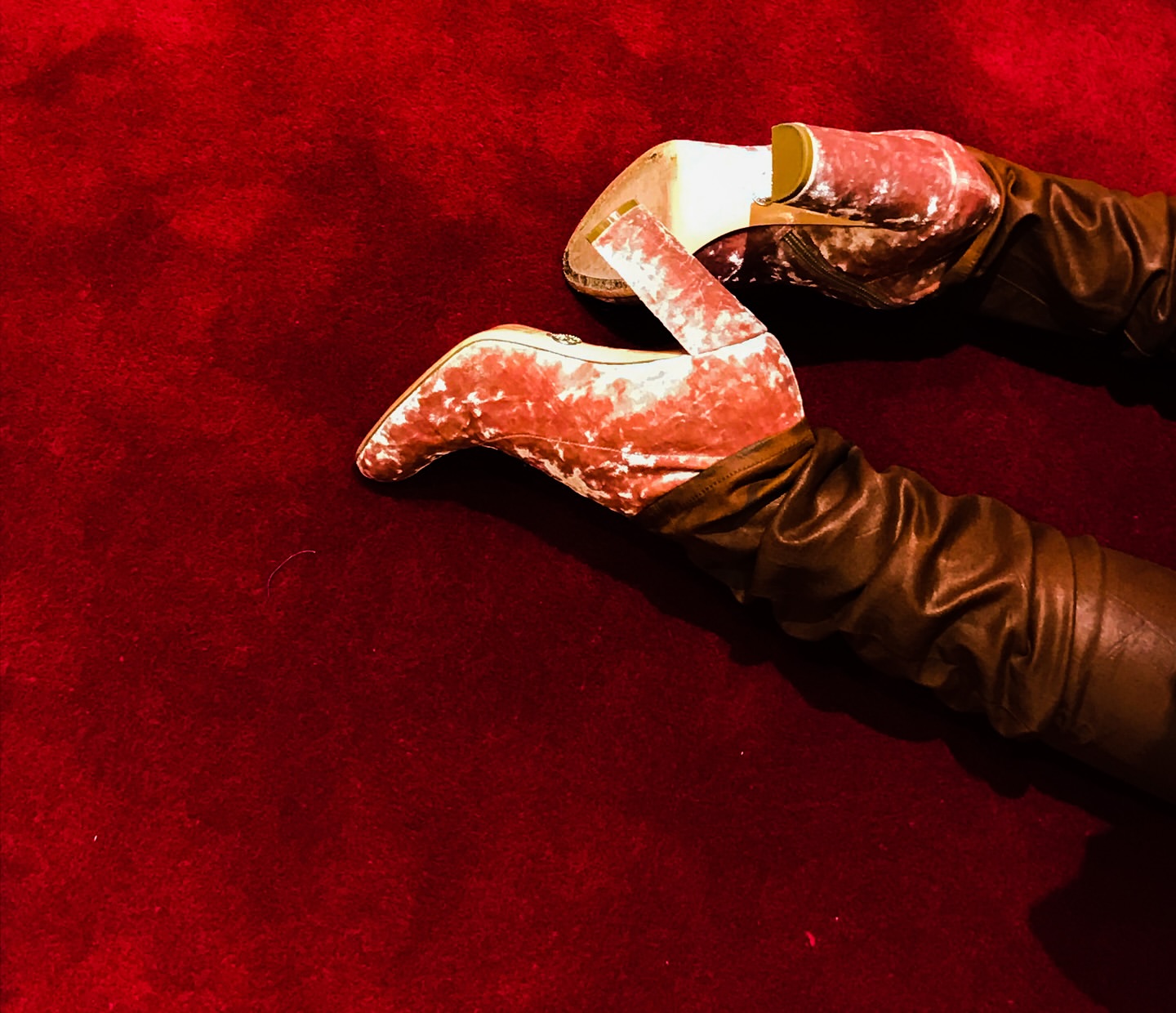 Fashion shot featuring velvet high heel shoes and leather gloves on a red velvet background. Focus on textures and material contrasts.