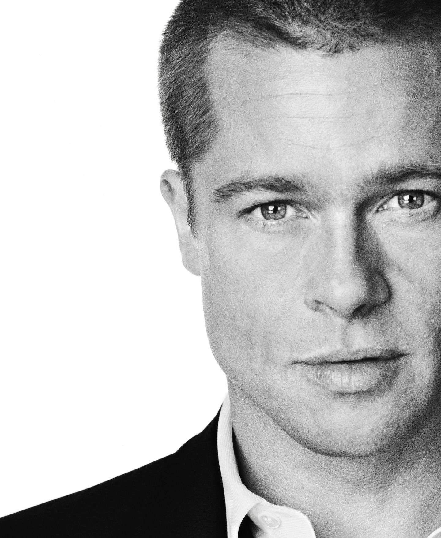 Close-up black and white portrait of Brad Pitt wearing a dark suit jacket and white shirt against a white background