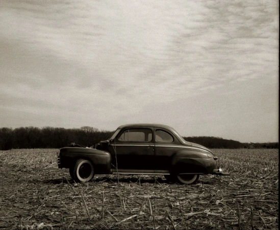 Vintage black car parked in a harvested cornfield under a cloudy sky, evoking a sense of rural nostalgia and classic automotive design.