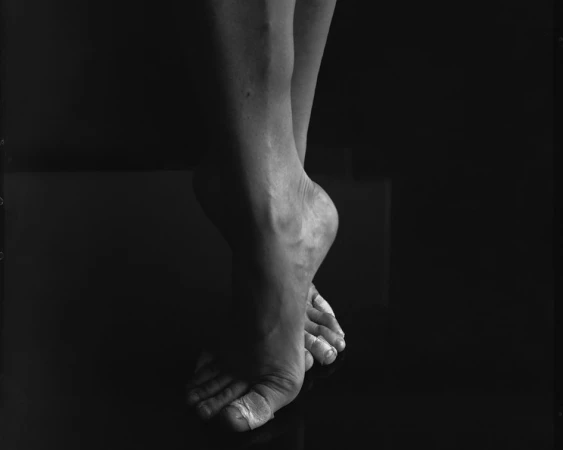 Black and white image of human legs and feet with crossed ankles, showing the human body on a reflective surface against a dark background.