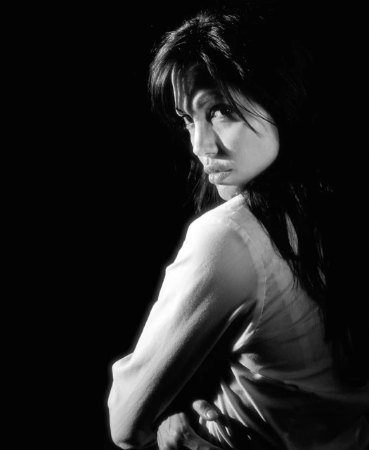 Monochrome portrait of an adult woman looking back over her shoulder with a neutral expression, against a dark background.