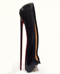 An extreme high-heeled black patent shoe with a thin red stiletto heel resting vertically against a plain white background.