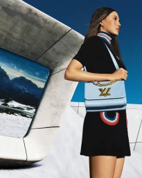 A woman wearing a black dress and holding a blue shoulder bag against a snowy mountain backdrop, produced by Giovanni Milano.