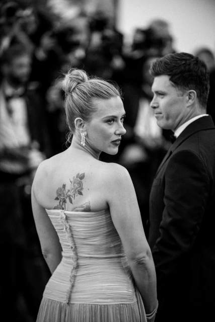 Black and white portrait of actress Scarlett Johansson in strapless dress with floral tattoo, accompanied by a man in a suit.