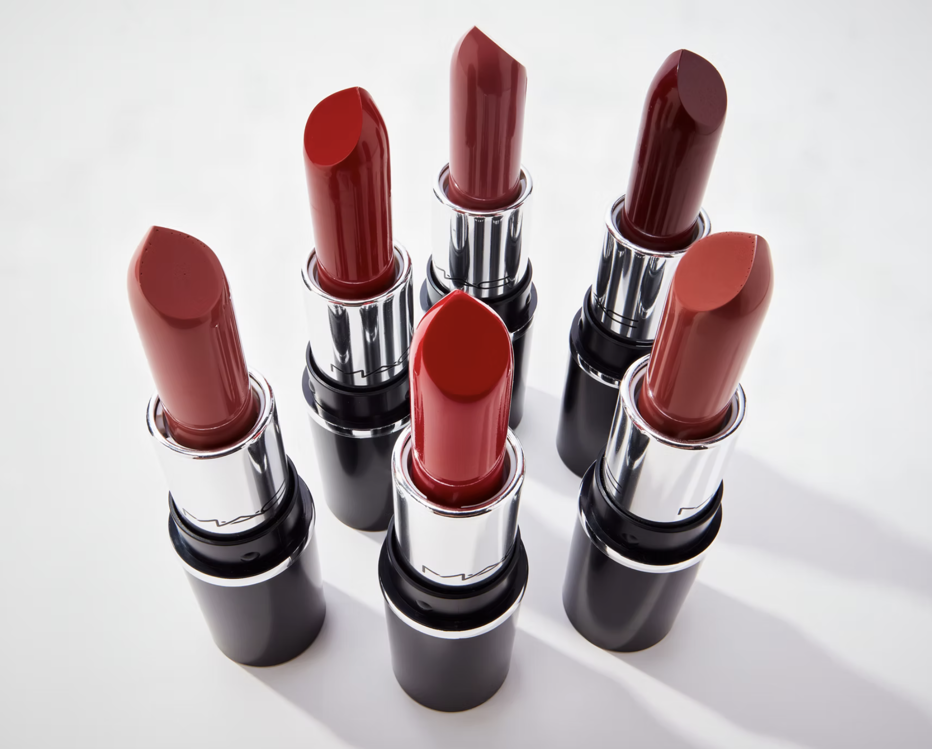 Assortment of red lipsticks with silver and black tubes arranged on a white surface, suitable for beauty or cosmetic themes.