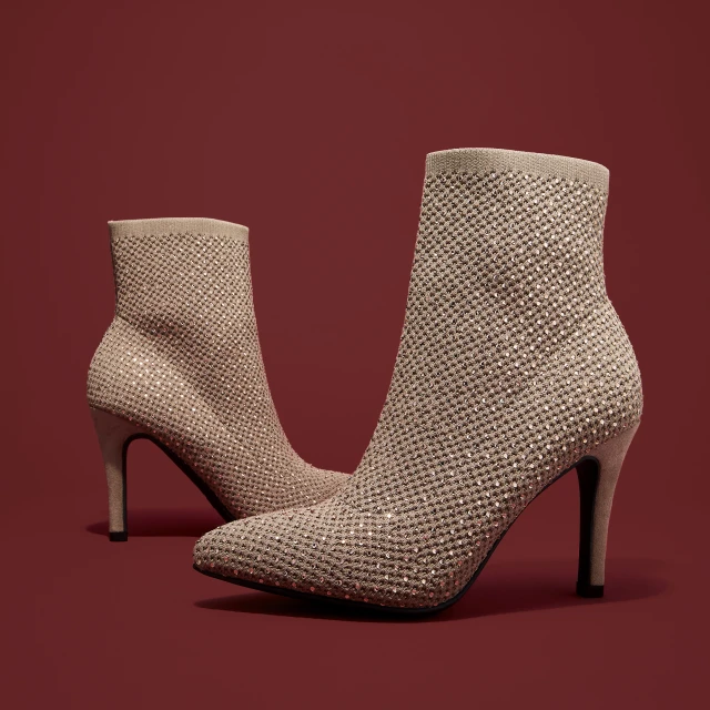 Beige sock-style high heel ankle boots embellished with rhinestones on a red background in a studio setting. Fashion footwear product shot.