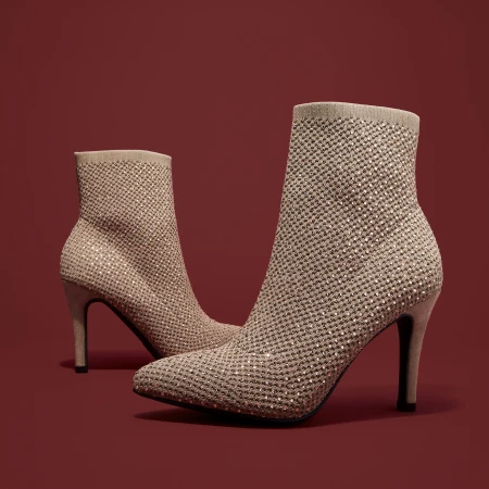 Beige sock-style high heel ankle boots embellished with rhinestones on a red background in a studio setting. Fashion footwear product shot.