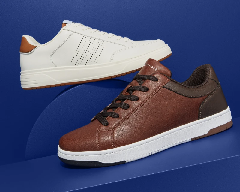 Two pairs of fashionable leather low-top sneakers, one white, one brown, presented on a blue surface for a fashion advertisement.