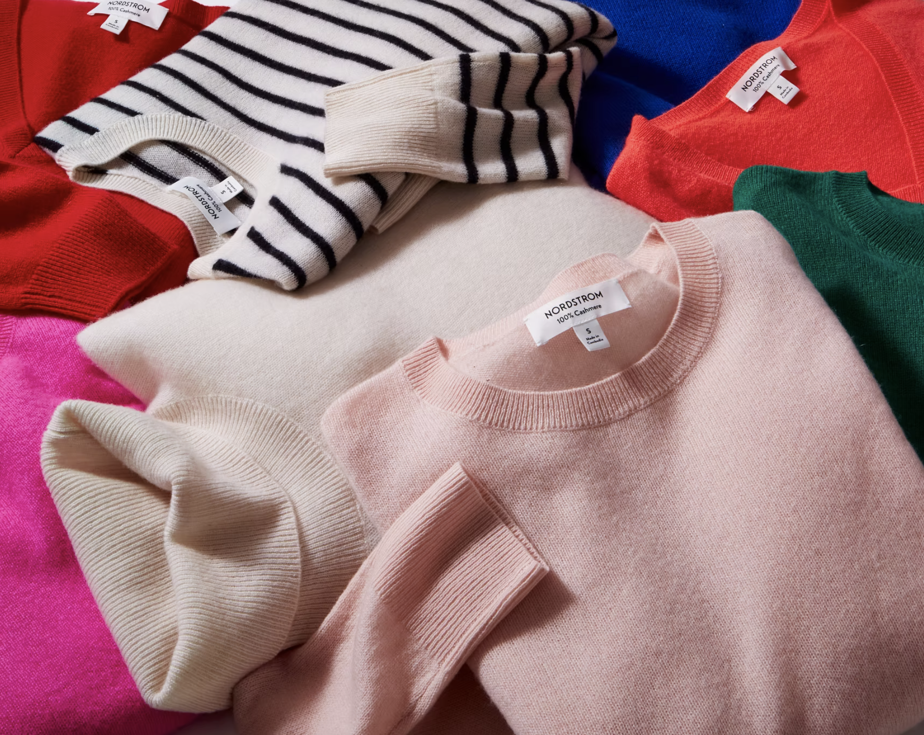 Collection of colorful cashmere sweaters in pink, red, green, blue, beige, and black-and-white stripes, neatly folded in a pile.