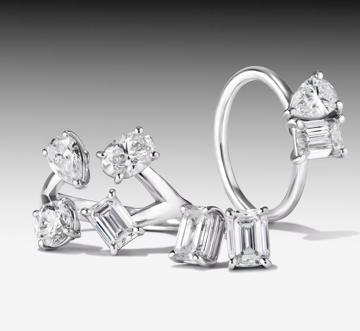 Close-up of various silver rings adorned with clear diamonds against a gradient gray background, showcasing elegant jewelry design.
