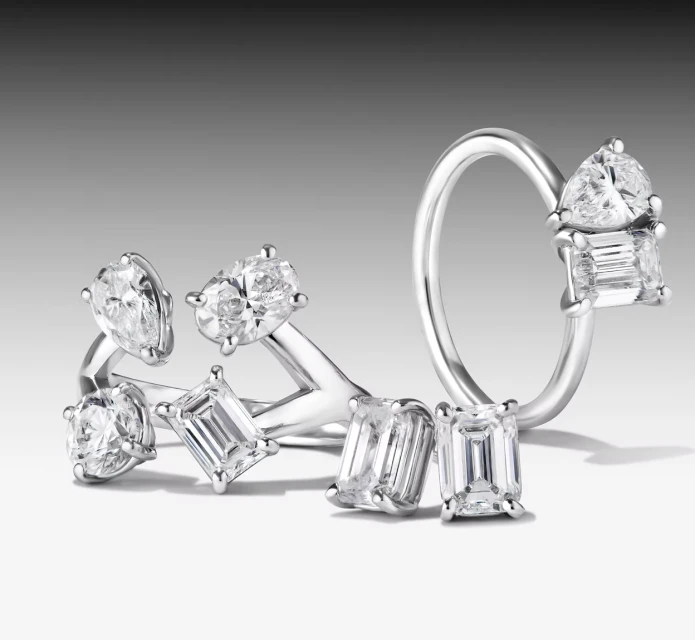Close-up of various silver rings adorned with clear diamonds against a gradient gray background, showcasing elegant jewelry design.
