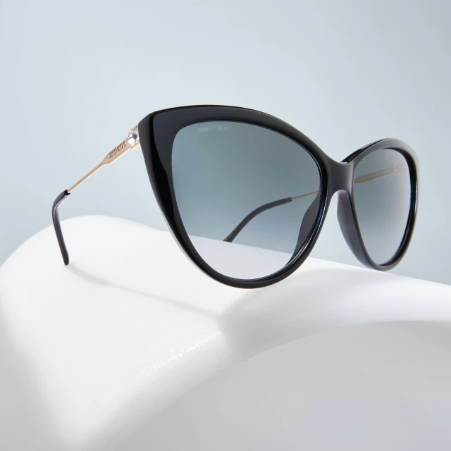 Close-up of black cat-eye sunglasses with gold arms on a white surface against a light blue background, showcasing fashion eyewear.