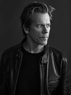 Portrait of actor Kevin Bacon wearing a leather jacket against a dark background