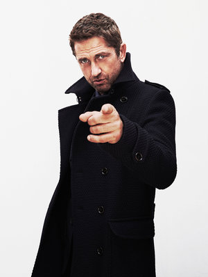 Adult male with brown hair, wearing a black coat, pointing directly at the viewer in a studio shot against a white background.