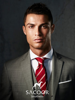 Close-up of a man in a grey suit and a red patterned tie, looking directly at the camera in a professional photo studio setting.