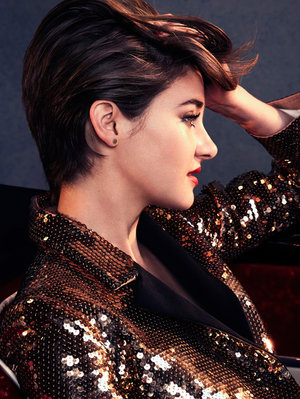 Portrait of a woman with short brown hair, wearing a sparkling gold jacket and red lipstick, captured in a medium shot from a side view.