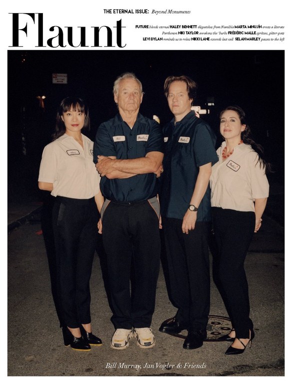 Four people standing outdoors at night on an asphalt street, wearing matching short-sleeved shirts and black trousers, featured on a magazine cover.
