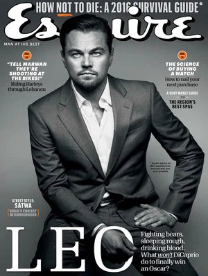 Leonardo DiCaprio wearing a tailored grey suit and white dress shirt against a plain grey background on a magazine cover.