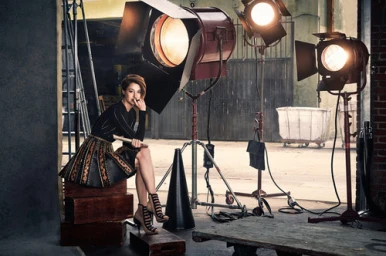 Musician Vanessa Perez seated on wooden crates among heavy studio stage lighting equipment in a New York workspace