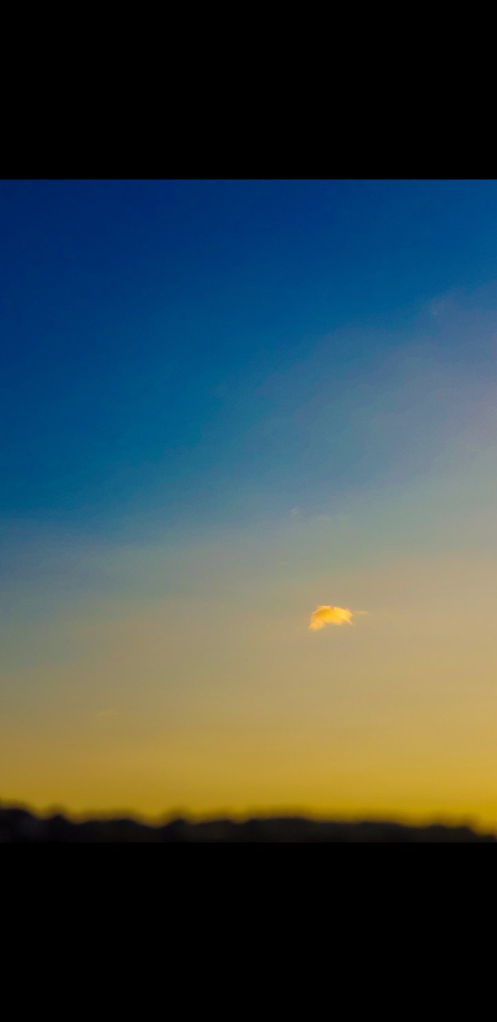 Sky at sunset features a gradient of deep blue to golden yellow, with soft clouds adding depth and texture to the vibrant atmospheric scene.